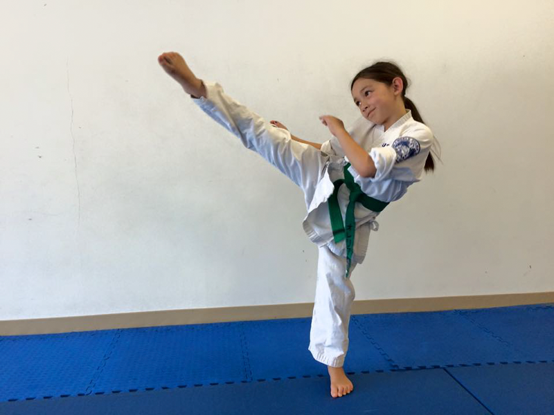 A green belt practices her roundhouse kick at kids class